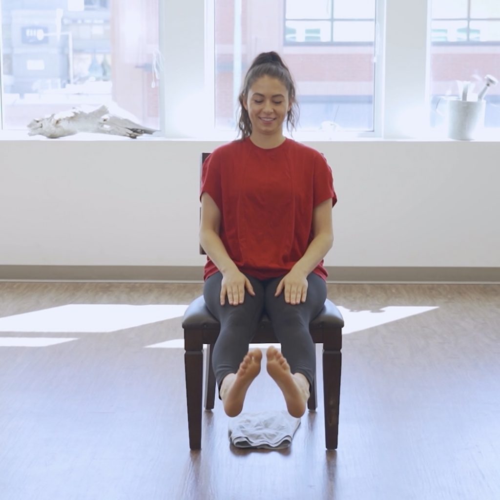 Senior seated on a chair performing ankle circles, rotating one foot in circular motions to improve ankle flexibility and strength, part of the 10 exercises to prevent falls.