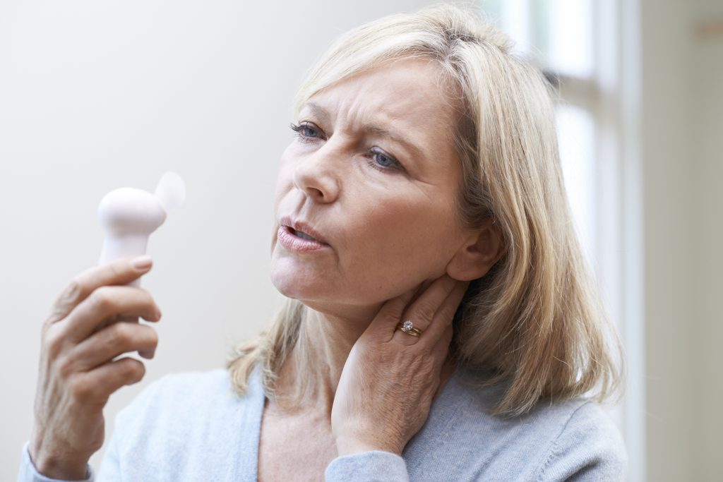 A senior woman suffers through a hot flash, using a small fan to help her cope–not realizing there are more effective natural remedies to help her.