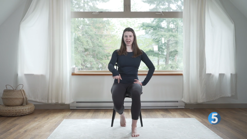 A fitness instructor is seated on a chair as she brings her heel back to finish off one rep of the Heel Drag leg exercise which helps in enhancing leg strength and flexibility, making it ideal for seniors.