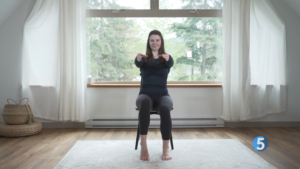 With her arms out in front of her the instructor pushes through her toes on one foot to raise her heel as another seated leg exercise in her routine