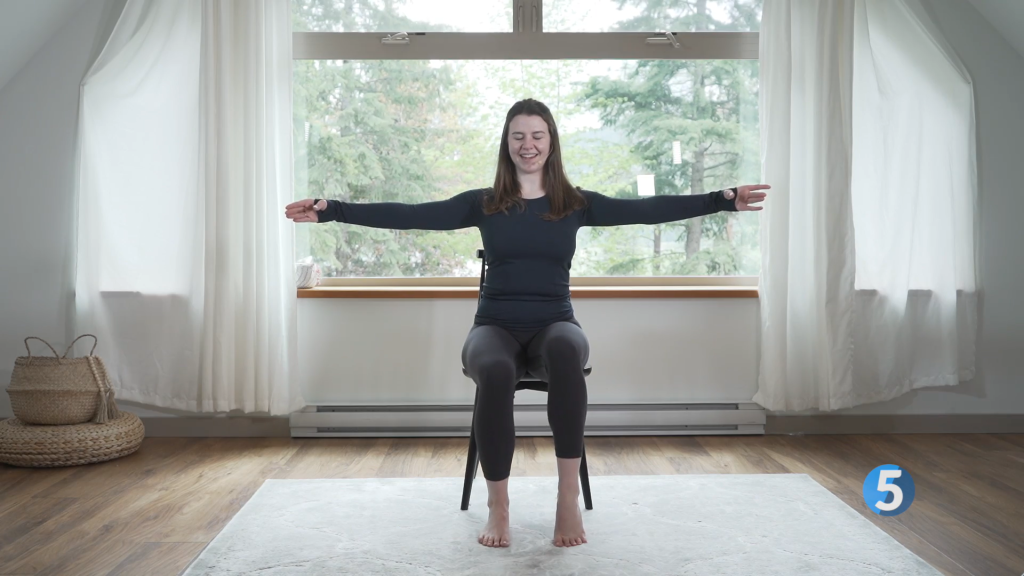 The instructor keeps her arms raised at her sides while bringing her first back down to lay flat and pushes her heel up on her other foot to finish off one rep of this seated leg exercise.