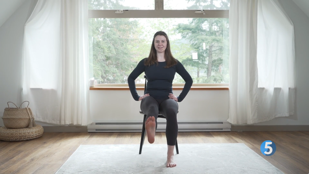 A fitness instructor is seated on a chair as she brings her heel back to finish off one rep of the Heel Drag leg exercise which helps in enhancing leg strength and flexibility, making it ideal for seniors.