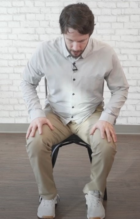 Instructor sitting on a chair, preparing to perform the sit-to-stand exercise, one of the easiest leg exercises for seniors