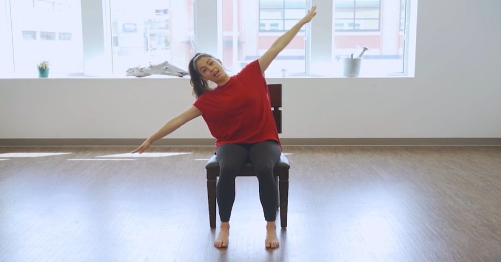 Instructor doing a seated chair Pilates side stretch for seniors to improve flexibility and mobility.