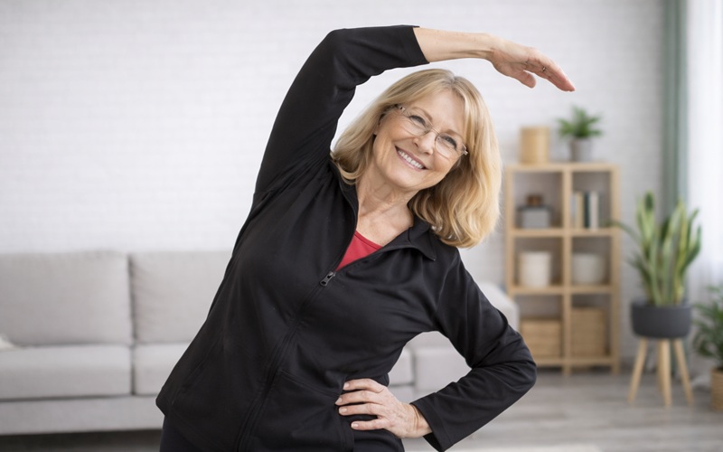 older adult smiling while doing gentle stretching exercises at home