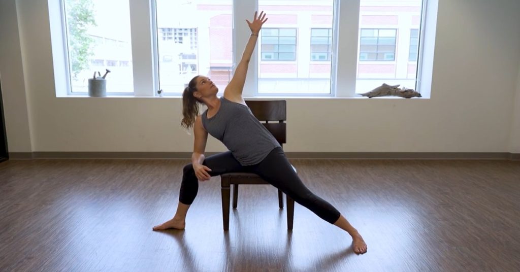 Female instructor demonstrating a gentle chair yoga pose for at-home exercise suitable for seniors.