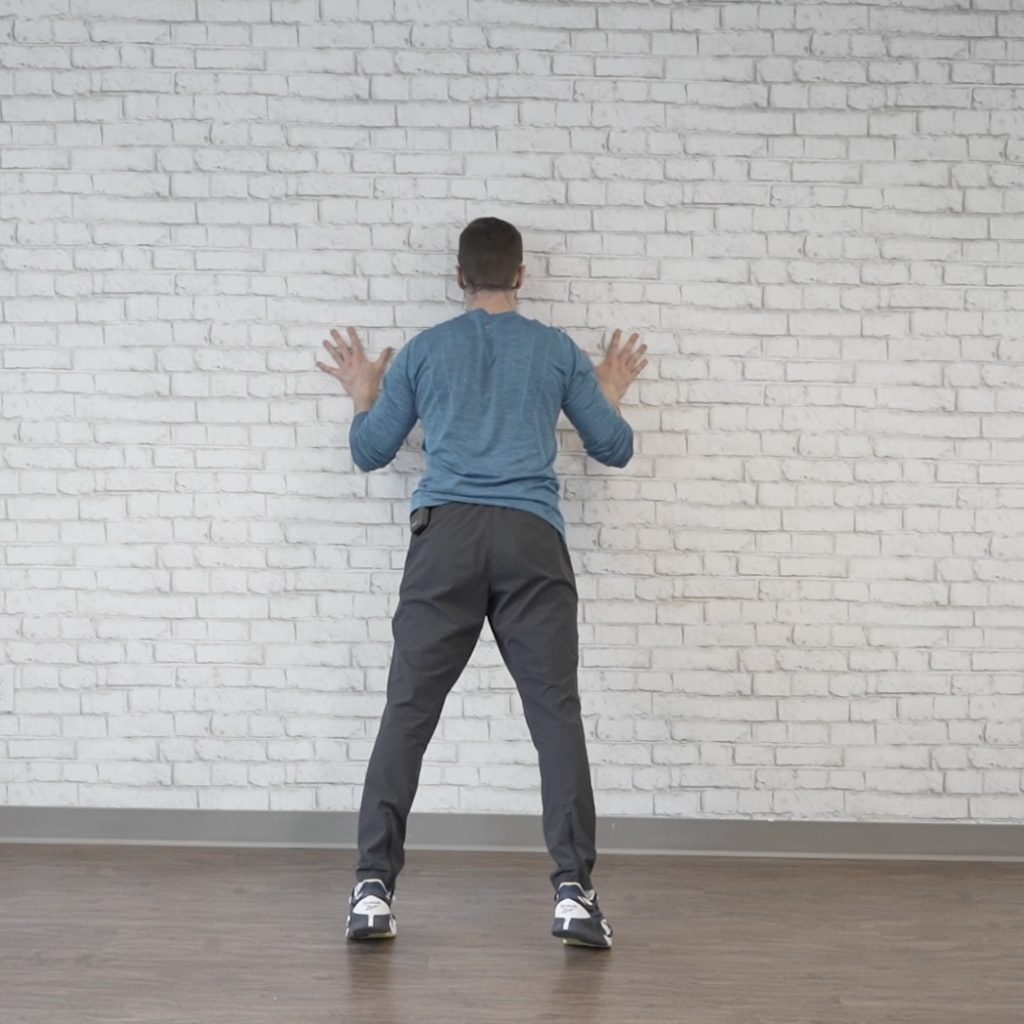 Fitness instructor demonstrates the downward motion of a wall push-up as part of an arm exercise routine.