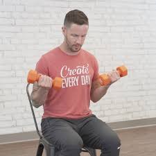 Fitness instructor performs seated bicep curls, holding orange dumbbells in both hands.