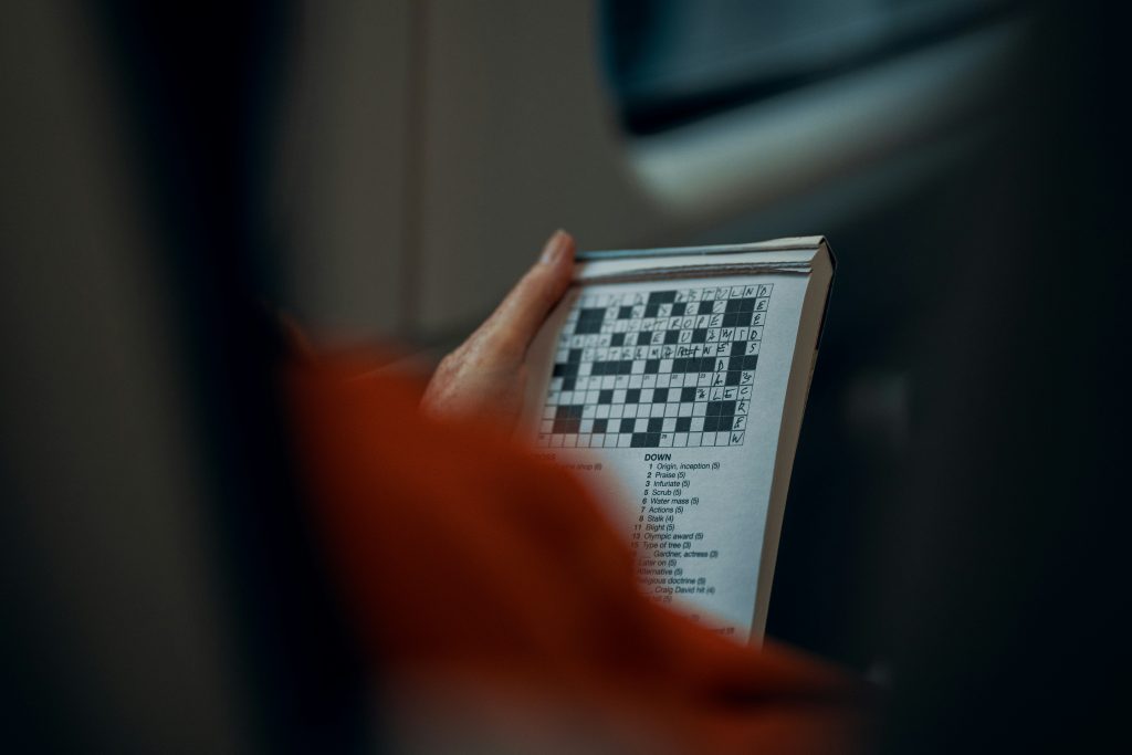 A senior holding a booklet while working on a crossword puzzle, one of the most popular memory games for seniors.