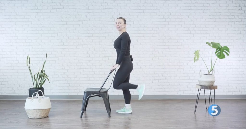 Female instructor performing chair-supported leg lift exercise for fall prevention and lower body strength