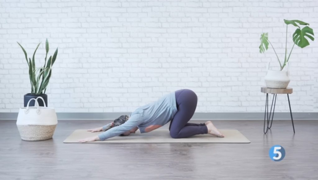 Woman performing child’s pose to stretch the back and shoulders as part of a gentle morning stretch routine.
