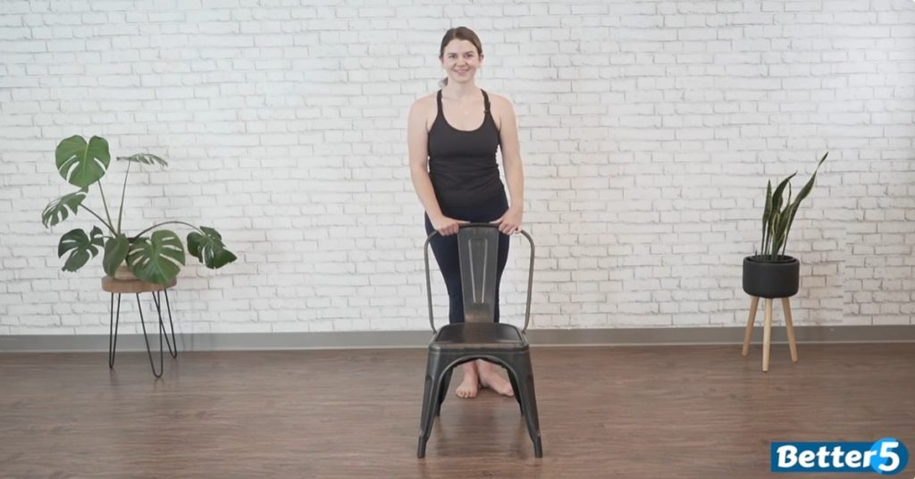 female instructor holding a chair for support while performing hip circles for balance and mobility