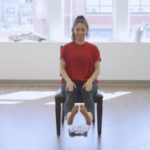 With both feet lifted off the ground, a woman demonstrates an ankle mobility routine, one of the exercises from the seated exercises for seniors PDF.