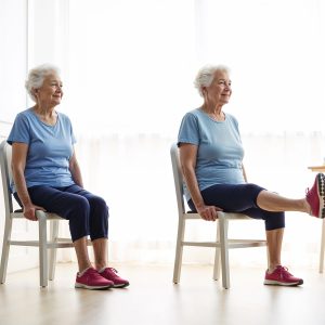 A senior woman performs seated leg extensions, a low-impact seated exercise for seniors.