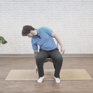 A man in a blue polo shirt performs a seated side bend to the left.