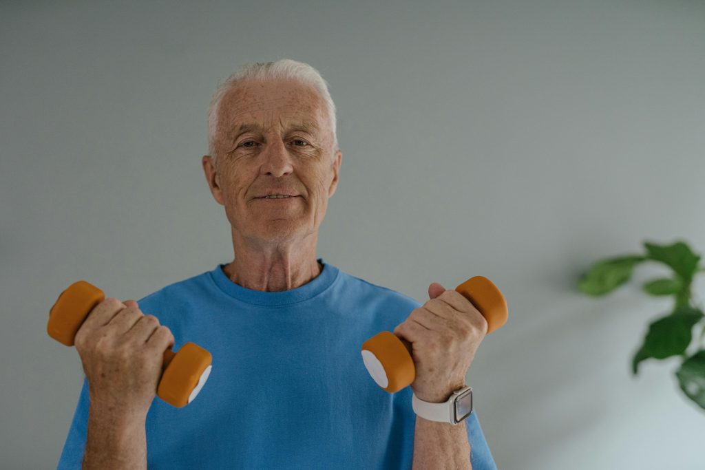 An older man holding small hand weights as part of a gentle workout routine to help reduce post-workout inflammation and improve recovery.