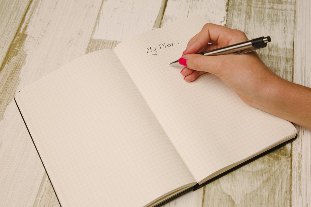 A hand holding a pen 'My Plan' in a notebook, representing the importance of knowing how to plan your day in retirement.