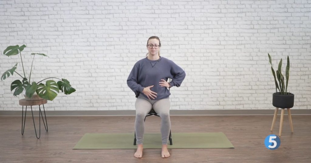 Yoga instructor demonstrating seated savasana relaxation for seniors in a gentle at-home exercise class