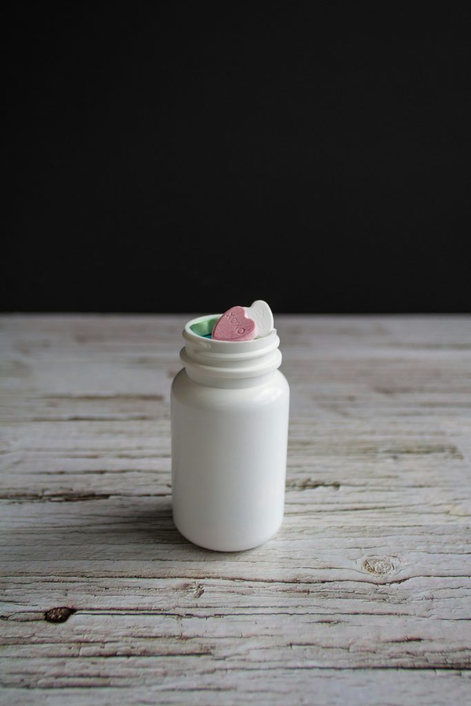 A white supplement bottle on a wooden surface with its partially open seal revealing pink and green tablets which can address nutrient deficiencies in older adults.